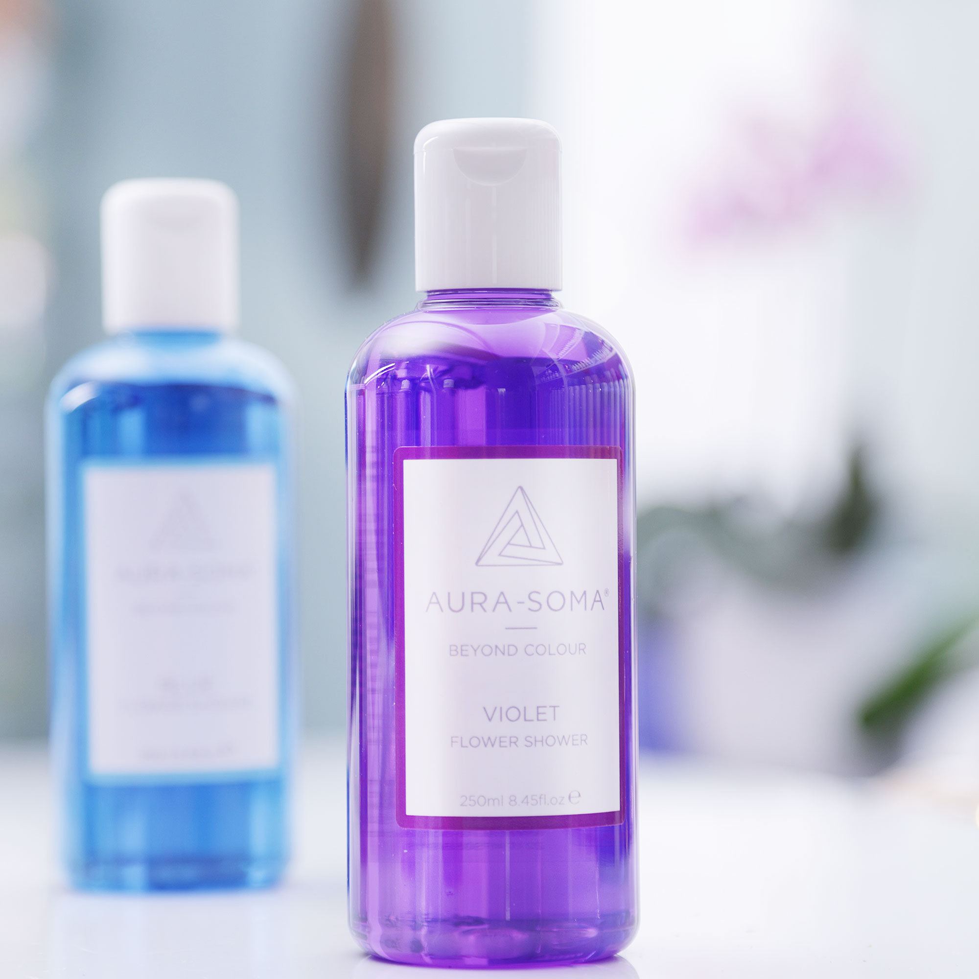 Aura-Soma Flower Shoer Violet Zwei Flaschen Duschbad von Aura-Soma, violett und Blau stehen in einem Badezimmer.